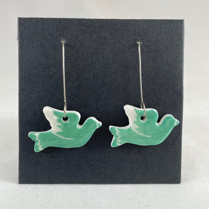 A pair of green porcelain earrings in the shape of flying dove on a black background.