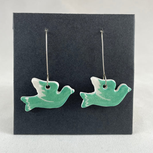 A pair of green porcelain earrings in the shape of flying dove on a black background.
