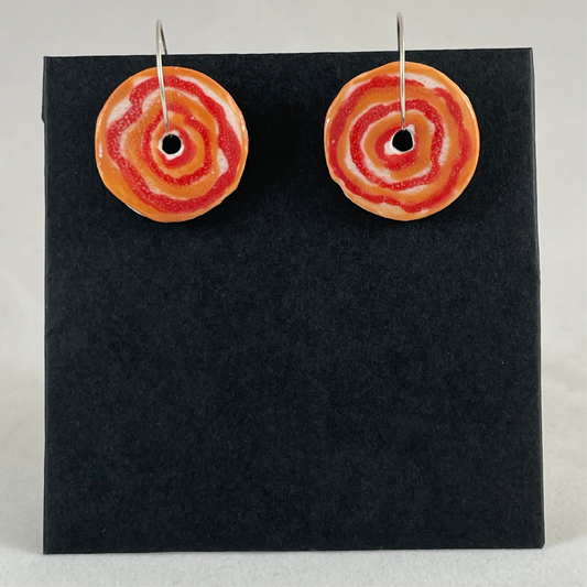 A pair of red and orange porcelain earrings on black card. box. Simple rose pattern with alternating, loosely painted red and orange circles.