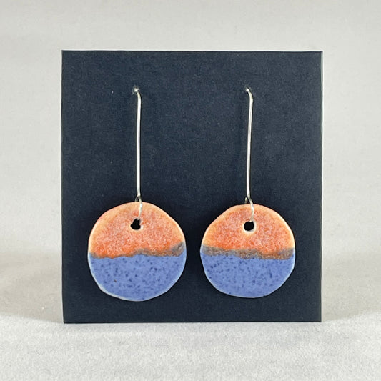 A pair of circular shaped porcelain earrings in blue and orange. On sterling silver earrings hooks.