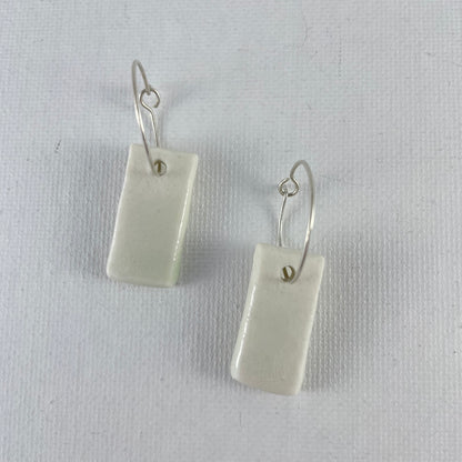A pair of silver hoops with hand formed white porcelain pendants laid flat on a white background.
