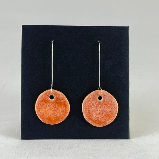 A pair of circular shaped porcelain earrings in bright orange. On sterling silver earrings hooks.