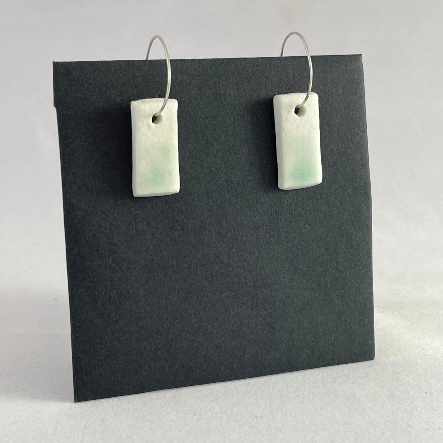 A pair of porcelain pendants in white with hint of green on a black background. Side view