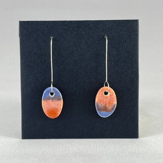 A pair of bright blue and orange oval earrings on a black background. 