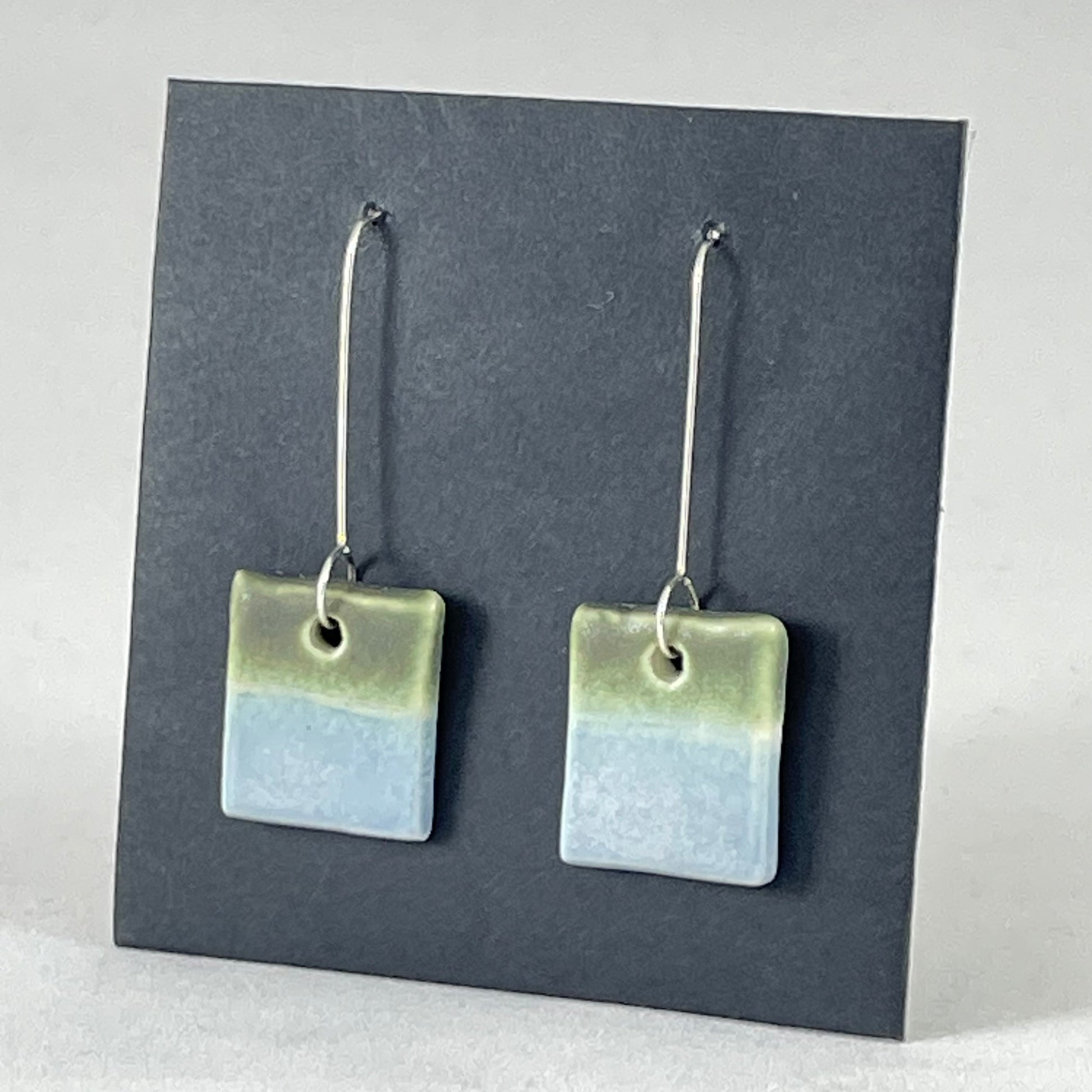 A pair of square shaped porcelain earrings in blue and green. On sterling silver earrings hooks. Side view