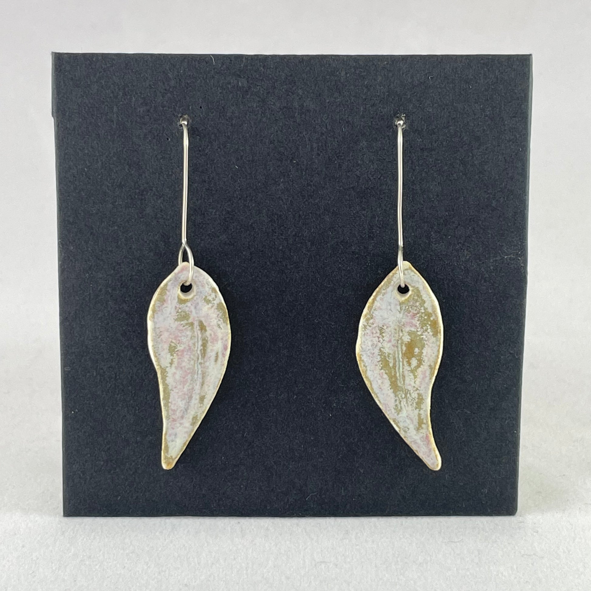 A pair of porcelain earrings in organic gum leaf shape. Photographed on a black background.