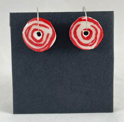 A pair of red and white porcelain earrings hanging on black card. Simple rose pattern with loosely painted red circles on white porcelain.
