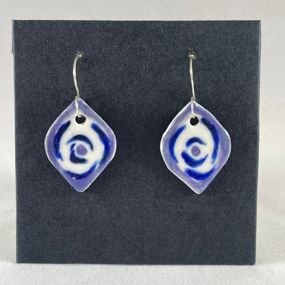 A pair of blue, lavender and white porcelain earrings hanging on black card. Pointed oval shape. Loosely hand painted blue circles on white porcelain, with a lavender border.