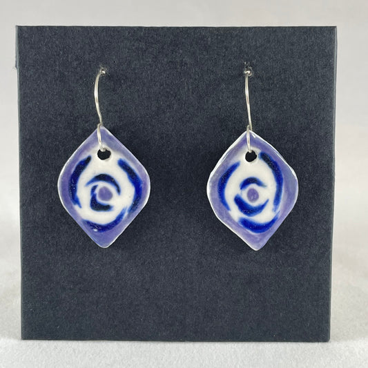 A pair of blue, lavender and white porcelain earrings hanging on black card. Pointed oval shape. Loosely hand painted blue circles on white porcelain, with a lavender border.