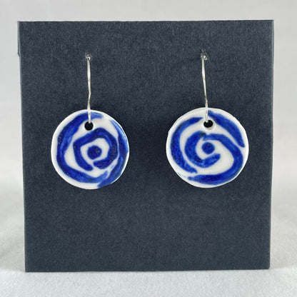 A pair of blue and white porcelain earrings hanging on black card. Simple rose pattern with loosely painted blue circles on white porcelain.
