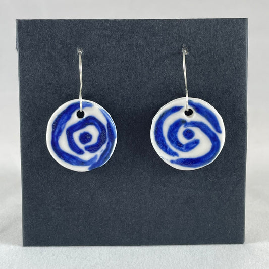 A pair of blue and white porcelain earrings hanging on black card. Simple rose pattern with loosely painted blue circles on white porcelain.