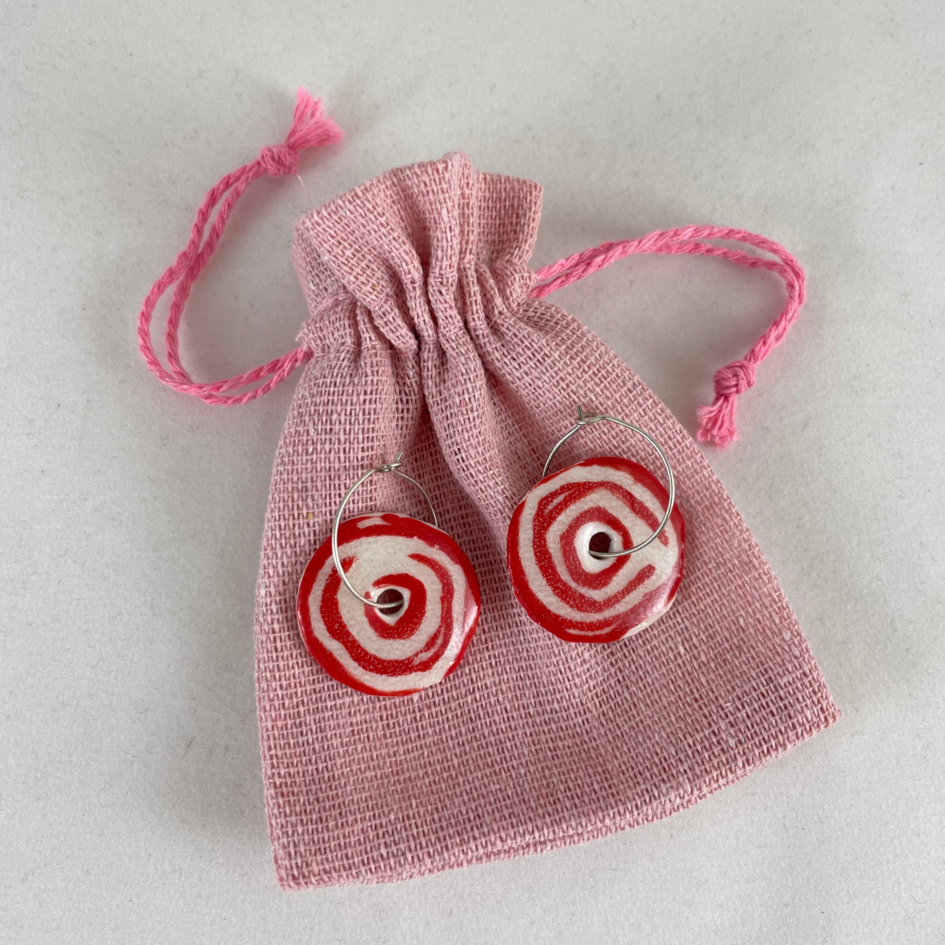 A pair of red and white porcelain earrings displayed on pale pink linen pouch.