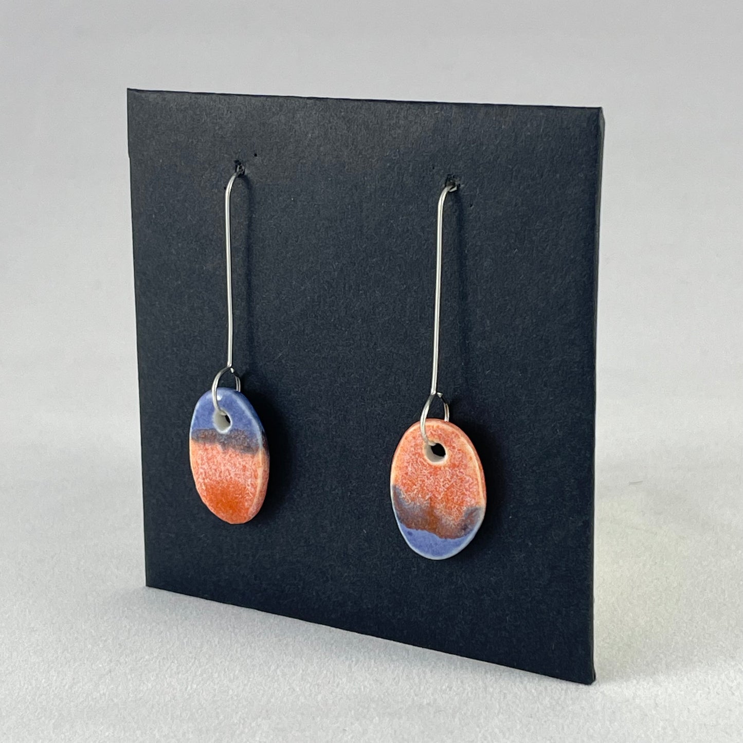A pair of bright blue and orange oval earrings on a black background. Side view 