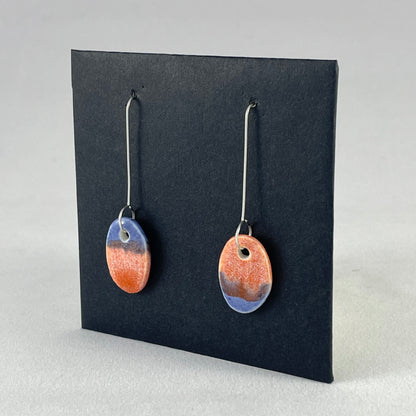 A pair of bright blue and orange oval earrings on a black background. Side view 