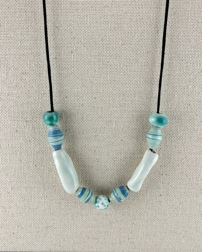 String of porcelain and paper beads on fine cotton thread. 4 paper beads with subtle stripes in light blue and pale green. 3 round porcelain beads in white and minty green, and two chunky pale green porcelain tube beads.