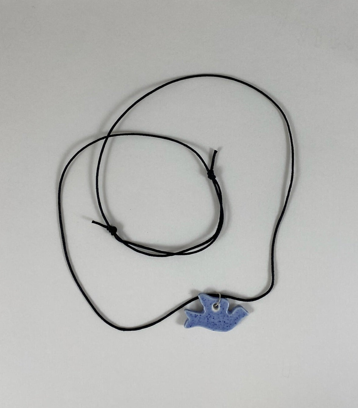 Necklace laid flat on white background. Fine black thread with dove shaped pendant in blue. Pendant is attached with small sterling silver jump ring.