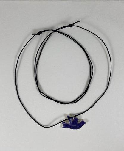 Necklace laid flat on white background. Fine black thread with dove shaped pendant in dark lavender purple. Fine white etchings on wing and tail. Pendant is attached with sterling silver jump ring.