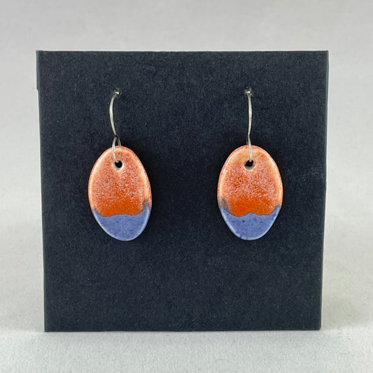 A pair of bright blue and orange oval earrings on a black background.