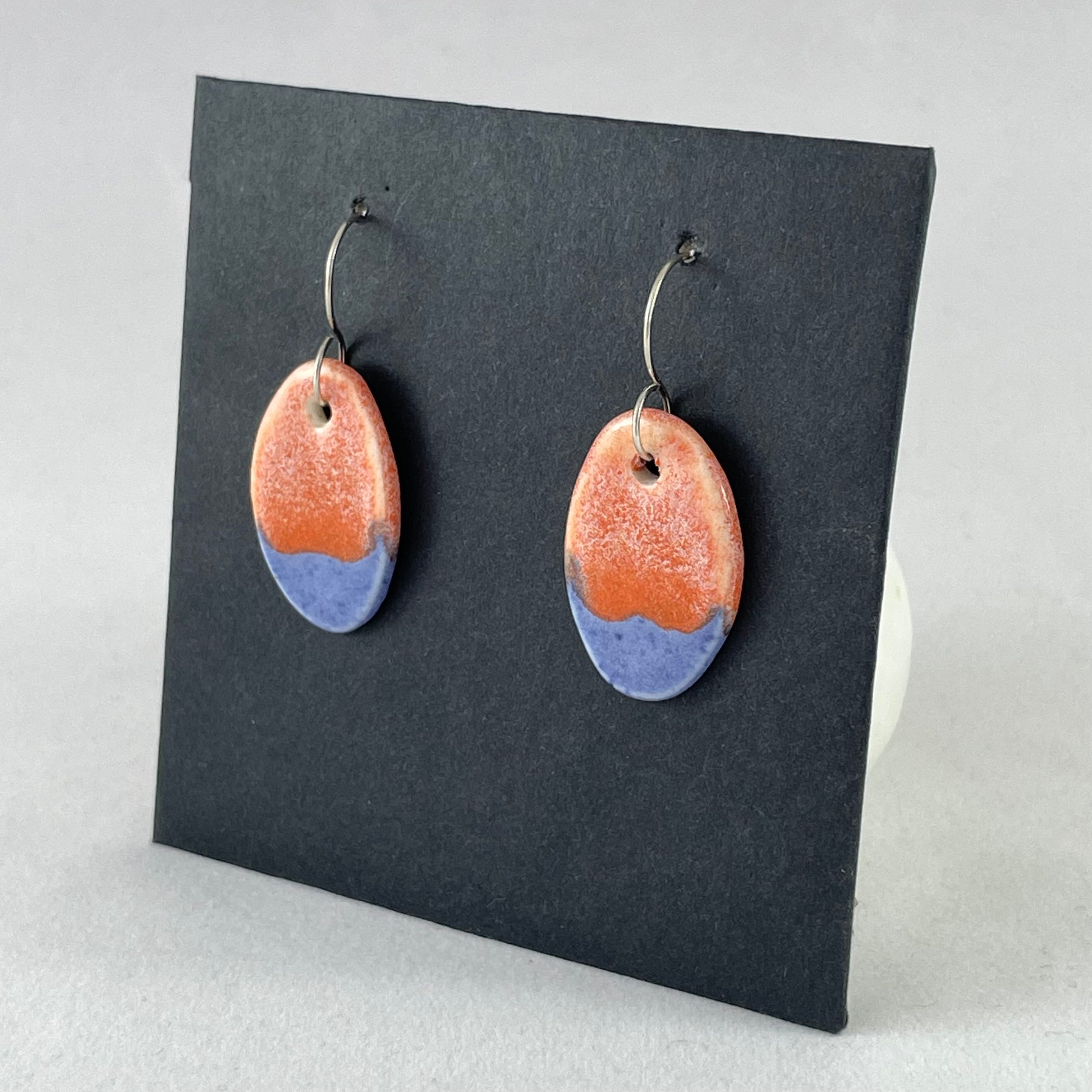 A pair of bright blue and orange oval earrings on a black background. Side view facing left