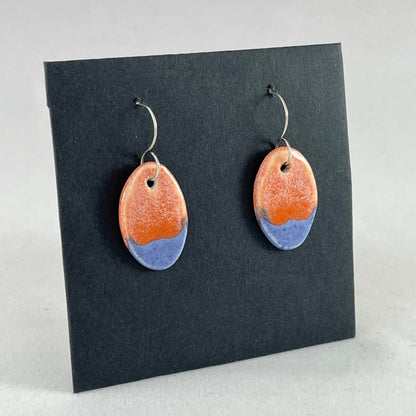A pair of bright blue and orange oval earrings on a black background. Side view facing right