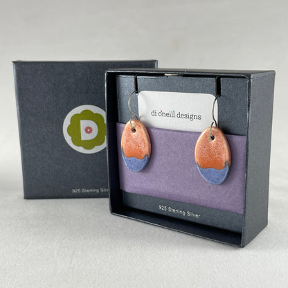 A pair of bright blue and orange oval earrings in a branded jewellery box with tissue paper.