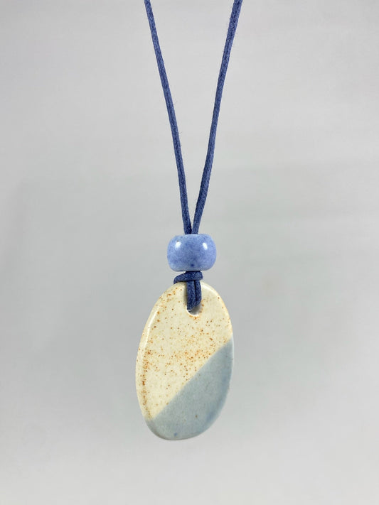 Necklace hanging against white background. Fine navy blue thread with pendant in cream with orange flecks and pale blue. A small pale blue porcelain bead sits above the pendant. 