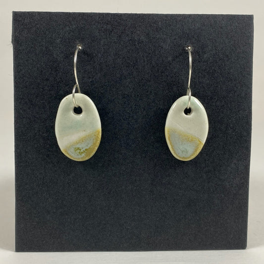 Fine rounded silver hooks with oval shaped pendants in white porcelain. Bottom half dipped asymmetrically in glaze speckled with light green, light brown and pale blue.  Top half has a very pale mint green glaze. Photographed on a black background. 