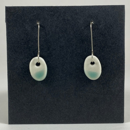 Fine silver hooks with oval shaped pendants in white porcelain. Bottom half  dipped in mint green shiny glaze, which fades  to white at the edges for a soft look.  Photographed on a black background.