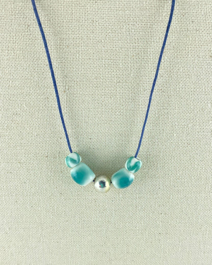 Two small round turquoise beads, two medium sized turquoise beads and a shiny silver bead in the middle. Thread on navy blue thread and photographed hanging against a cream linen background