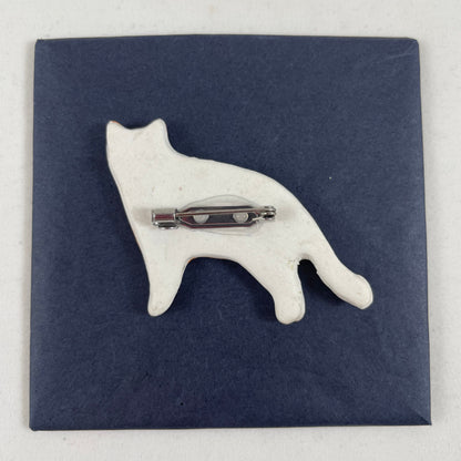 Back view of brooch. White unglazed porcelain with stainless steel brooch fastening glued on.