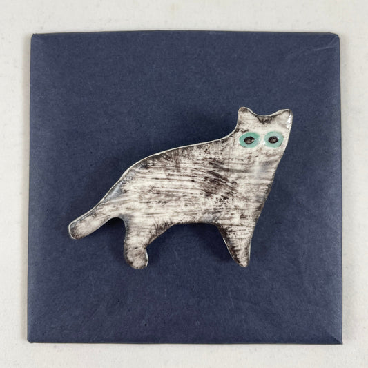 White cat brooch with fine black brush strokes. Effect is grey from a distance or black and white close up. Large green eyes. Photographed on black background.