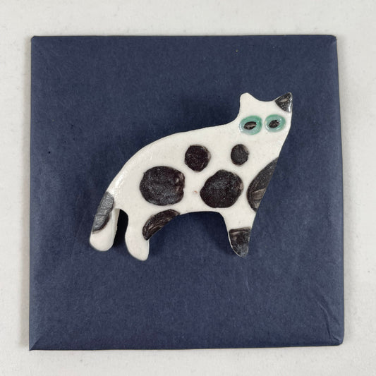 White porcelain cat with large irregular black spots and patches. Large green eyes. Photographed flat on a black background.