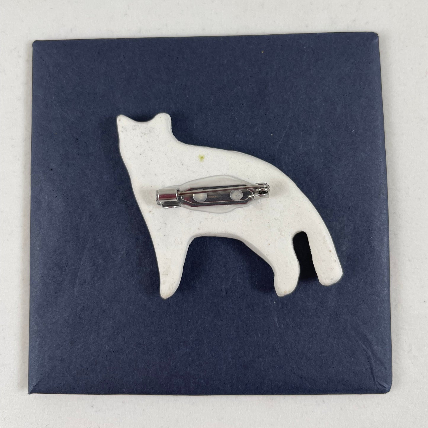 Back view of brooch. White unglazed porcelain with stainless steel brooch fastening glued on.