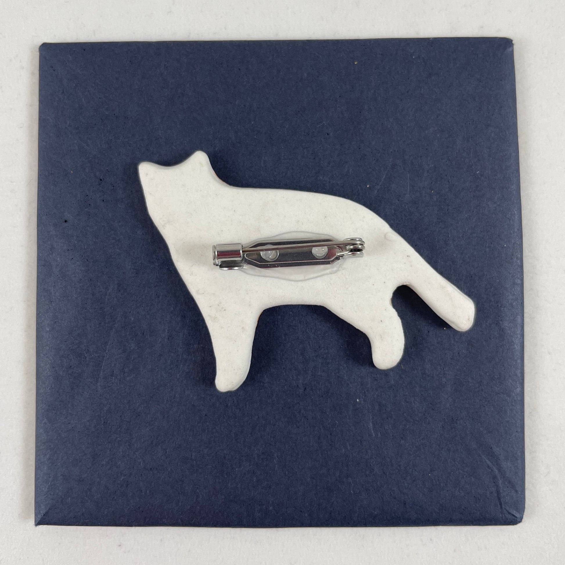 Back view of brooch. White unglazed porcelain with stainless steel brooch fastening glued on.