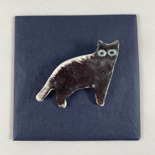 Black porcelain cat. Spiky black brush strokes on its back look like hairs standing on end. Large green eyes. Photographed flat on a black background.