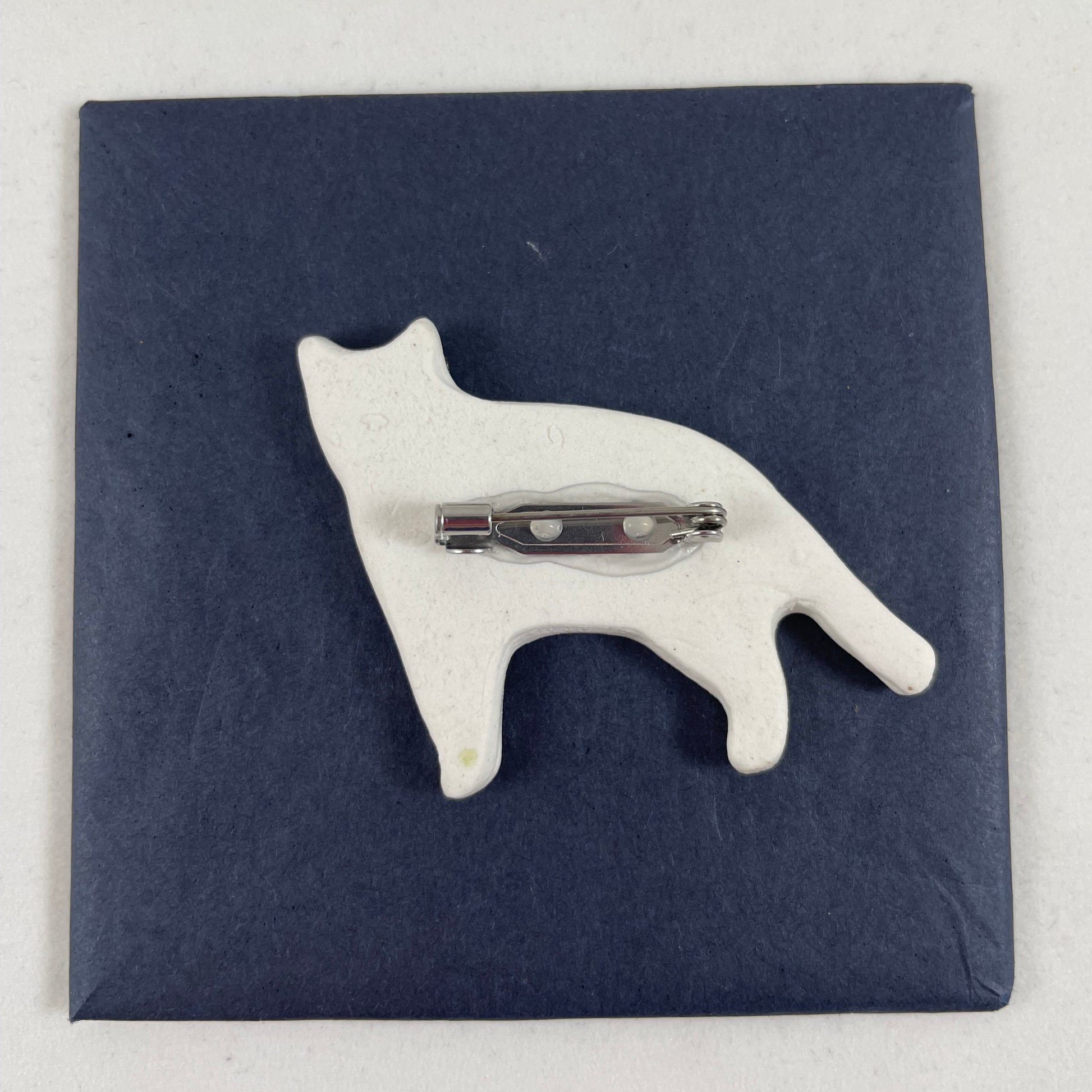 Back view of brooch. White unglazed porcelain with stainless steel brooch fastening glued on.