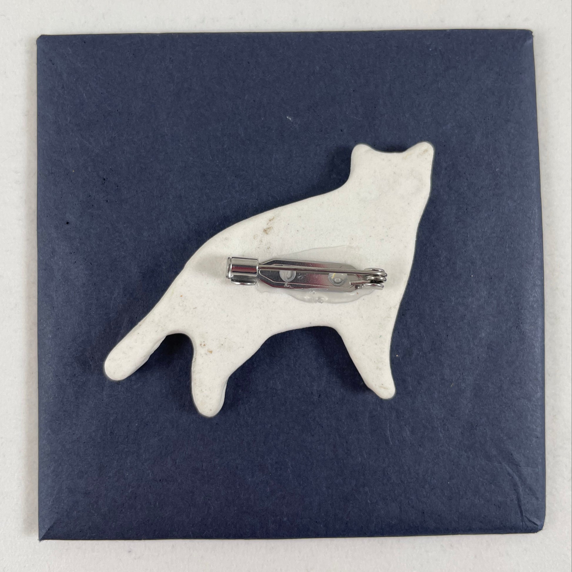 Back view of brooch. White unglazed porcelain with stainless steel brooch fastening glued on.