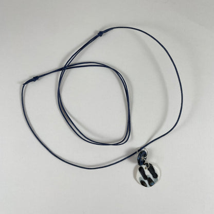 Necklace laid flat on white background. Fine black string with two circular porcelain pendants attached with silver jump rings. One pendant is small and navy blue and the larger pendant is white with navy glaze drips that looks like watercolour paint.