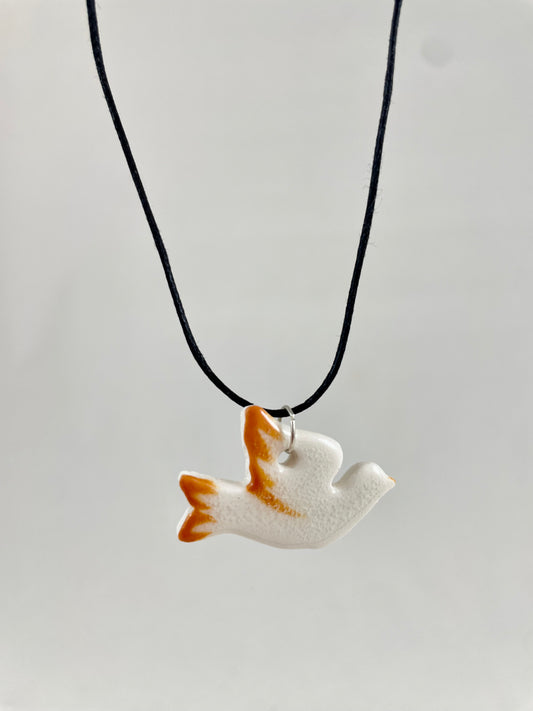 Necklace hanging against white background. Fine black thread with dove shaped pendant in white with orange wing and tail. Pendant is attached with small sterling silver jump ring.