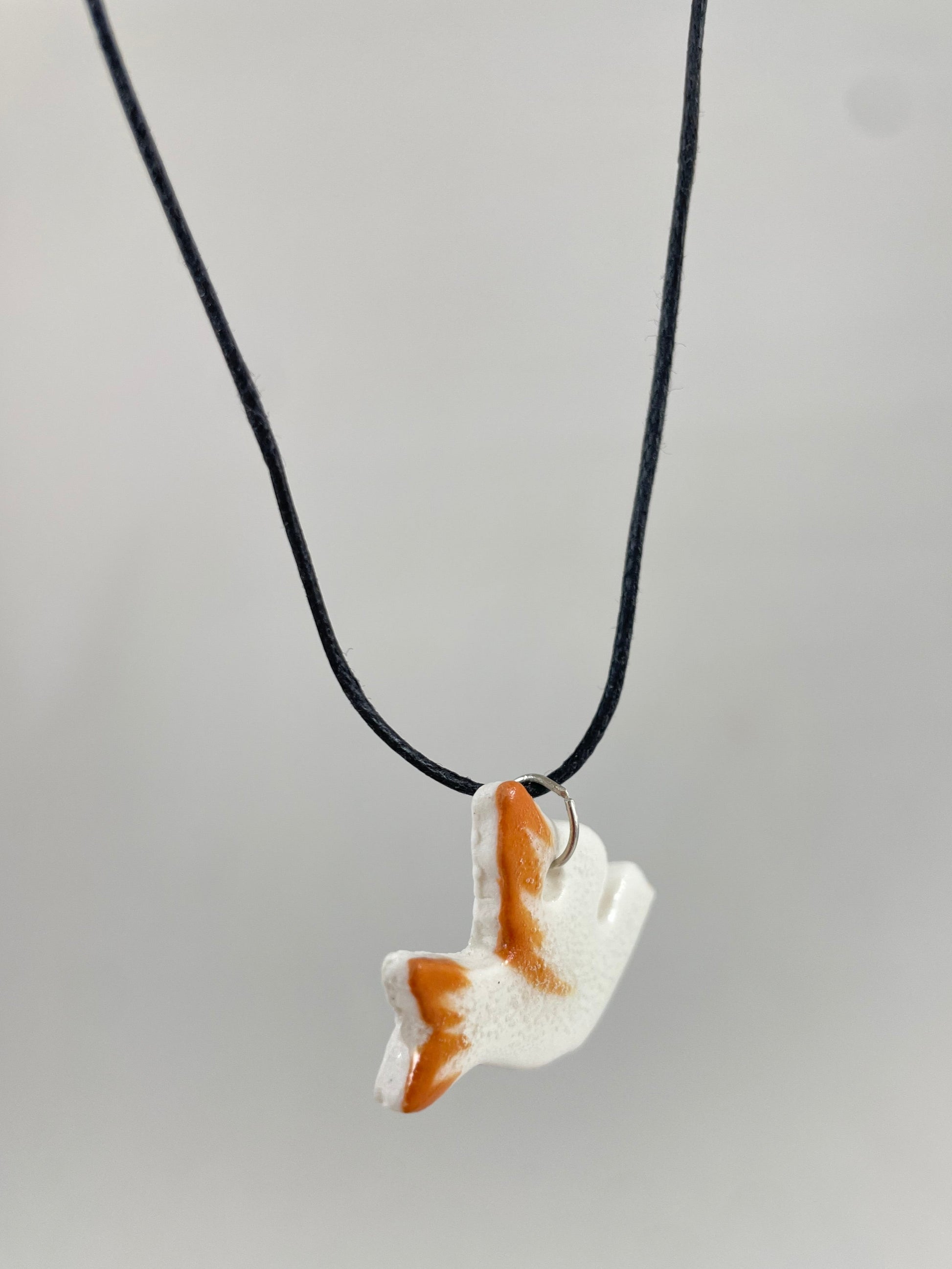 Necklace hanging against white background. Fine black thread with dove shaped pendant in white with orange wing and tail. Pendant is attached with small sterling silver jump ring. Side view taken from left hand side. Porcelain pendant is thin.