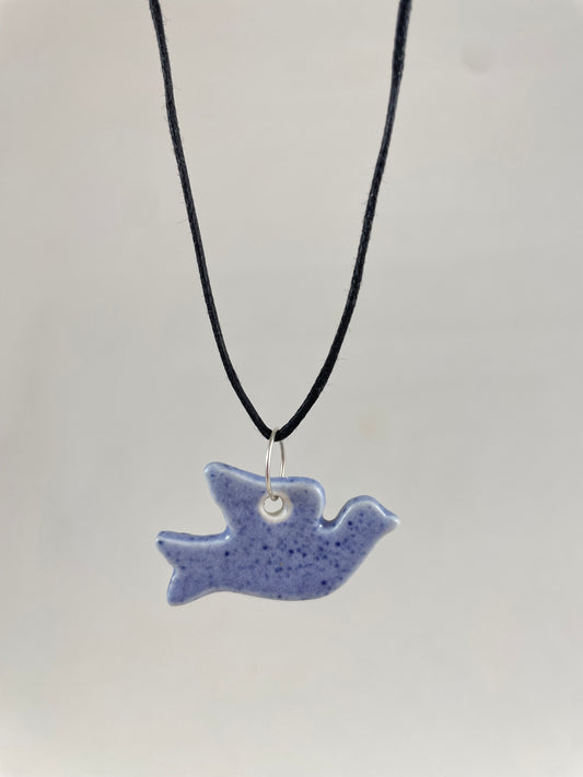 Necklace hanging against white background. Fine black thread with dove shaped pendant in pale blue with dark blue flecks. Pendant is attached with small sterling silver jump ring.