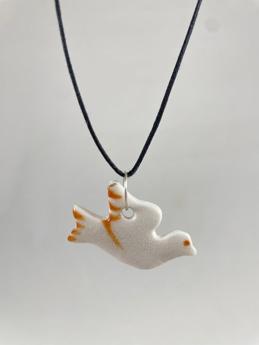 Necklace hanging against white background. Fine black thread with dove shaped pendant in white. Fine bright orange brush strokes on wing and tail. Pendant is attached with small sterling silver jump ring.