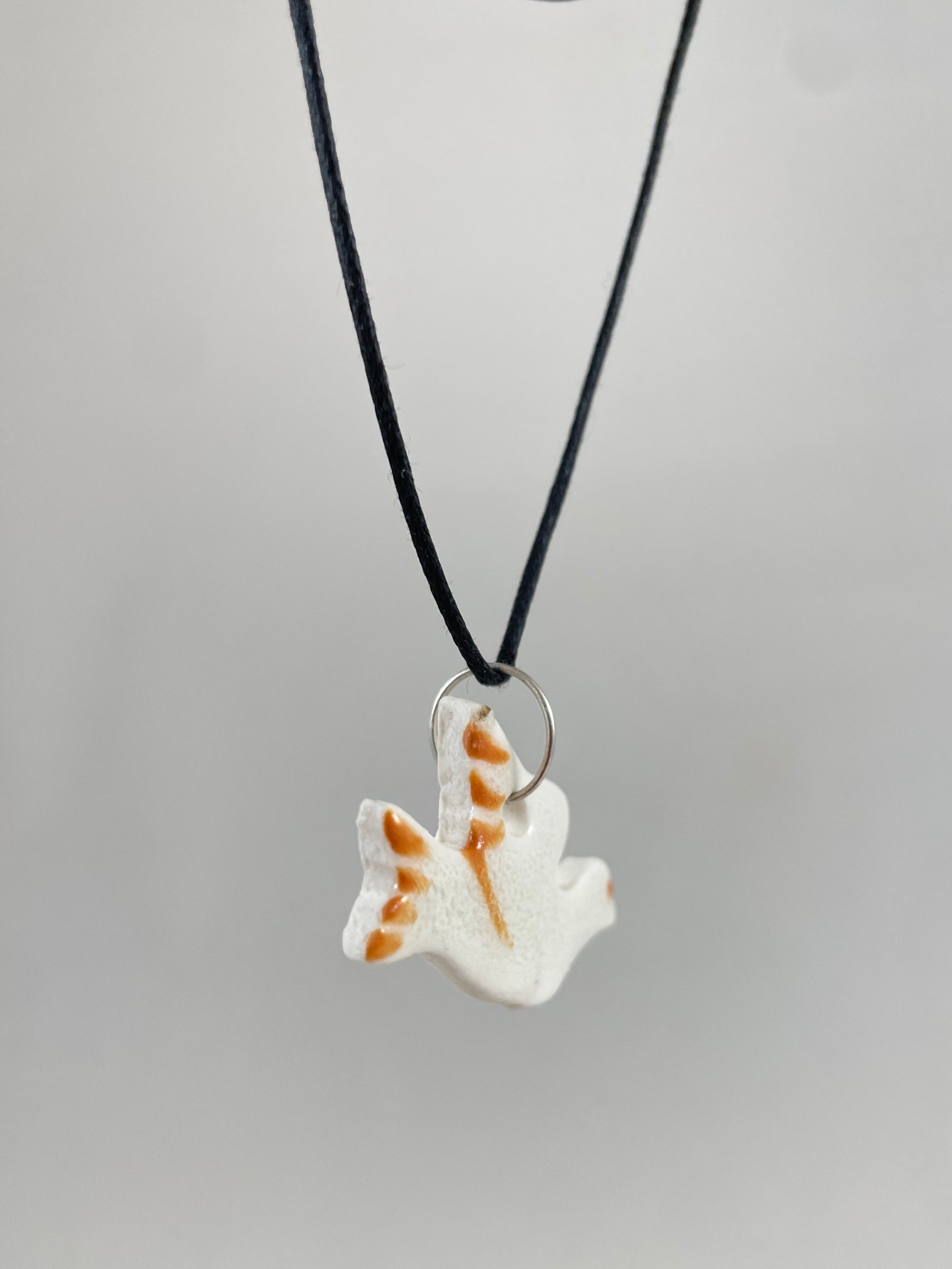 Necklace hanging against white background. Fine black thread with dove shaped pendant in white. Thin bright orange brush strokes on wing and tail. Pendant is attached with small sterling silver jump ring. Side view. Pendant is made of thin porcelain.