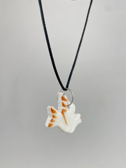 Necklace hanging against white background. Fine black thread with dove shaped pendant in white. Thin bright orange brush strokes on wing and tail. Pendant is attached with small sterling silver jump ring. Side view. Pendant is made of thin porcelain.