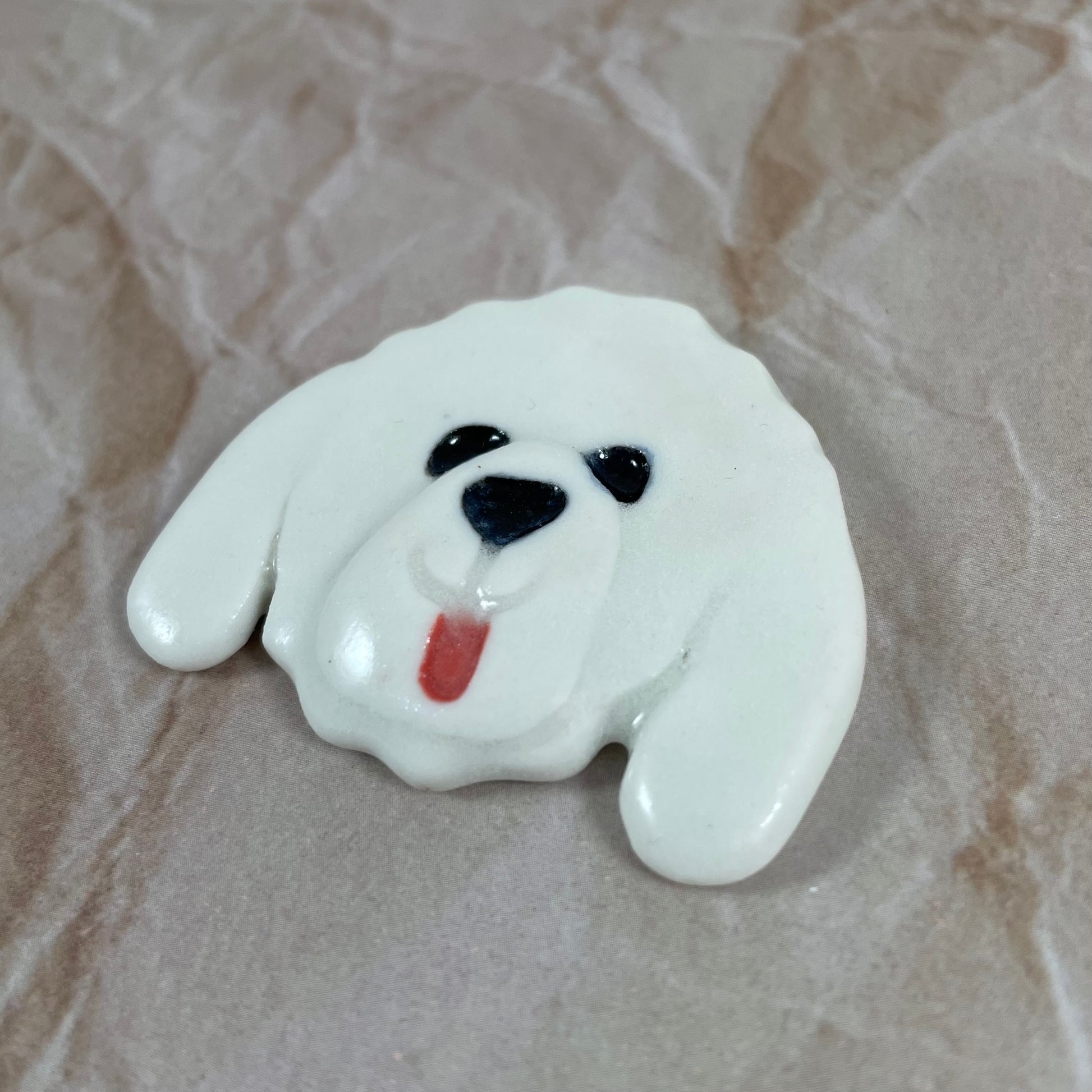 Dog's head in glossy white porcelain with long ears and rosy pink tongue sticking out. Shiny black eyes and nose. Muzzle area is slightly raised to stand out. Photographed from right hand side. Porcelain is thin
