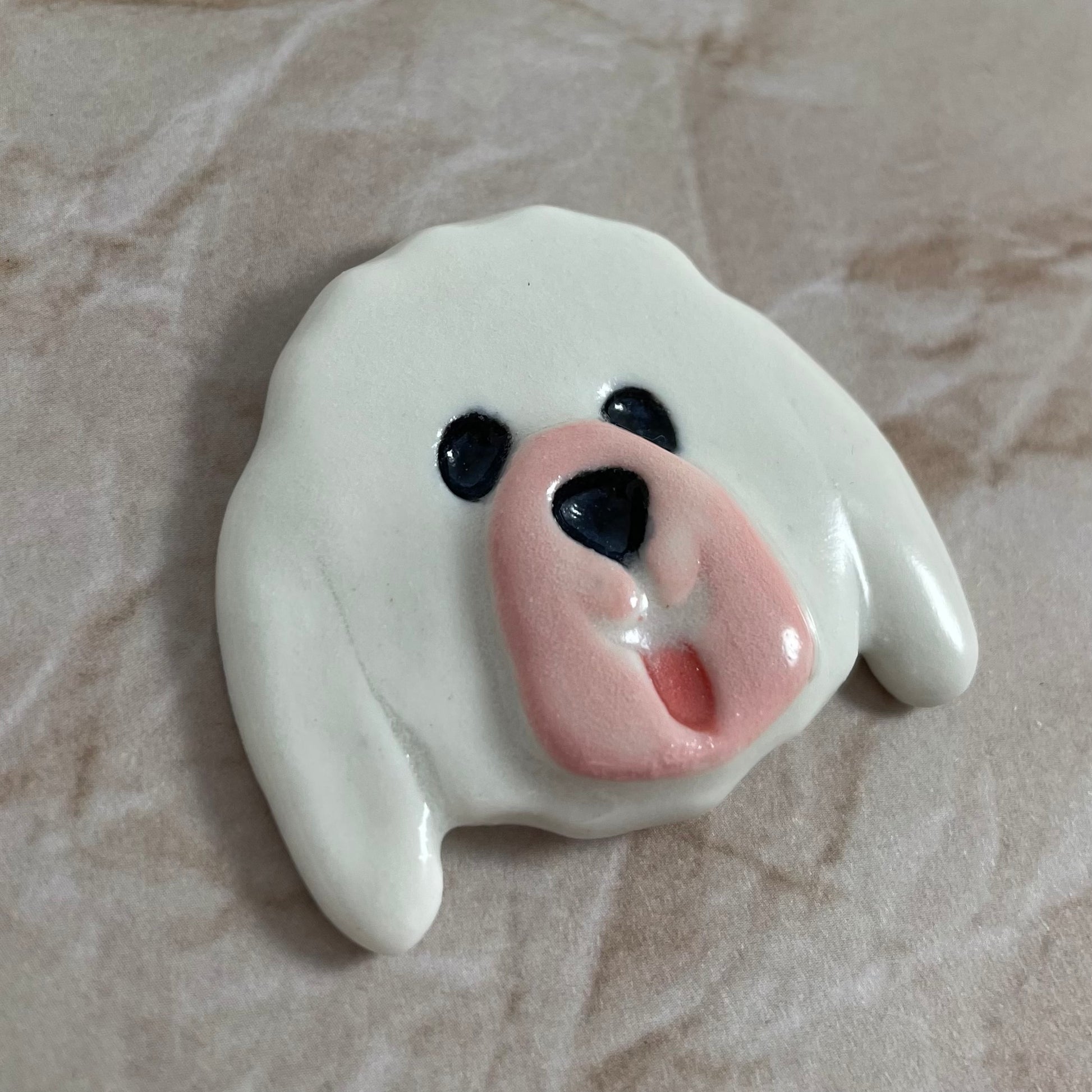 Dog's head in glossy white porcelain with long ears and rosy pink tongue sticking out. Shiny black eyes and nose. Muzzle area is pale pink and slightly raised to stand out. Photographed from left hand side. Porcelain is thin