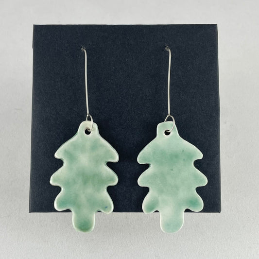 A pair of handmade porcelain earrings in oak leaf shape and glossy mint green glaze. Photographed on a black background. On sterling silver earrings hooks.