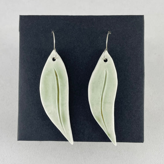 A pair of hand formed porcelain earrings in organic gum leaf shape. Photographed on a black background. On sterling silver earrings hooks.